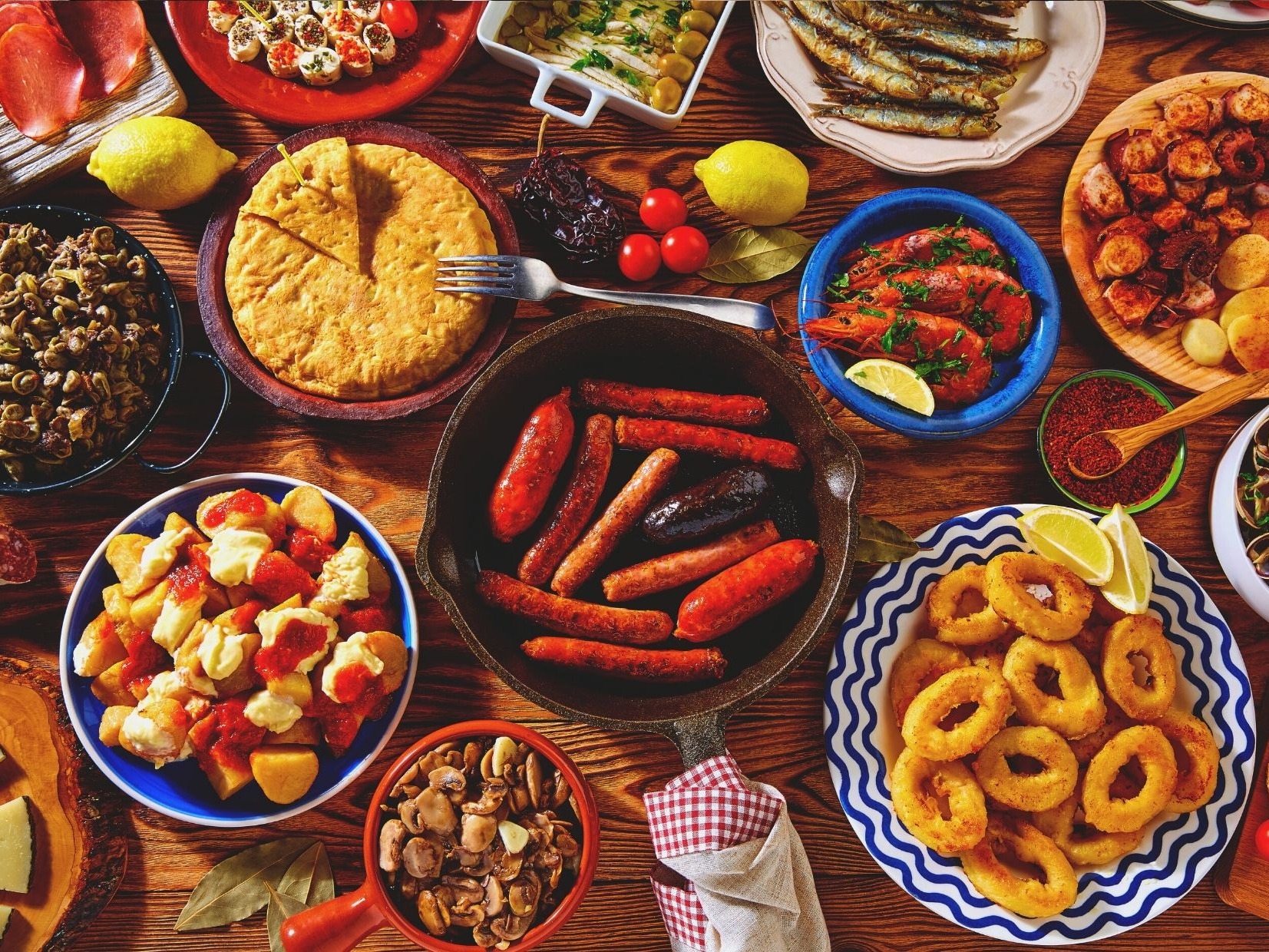 A Spanish cuisine cookbook cover with tapas, paella, seafood, rustic breads, and bright Mediterranean-style flavors.