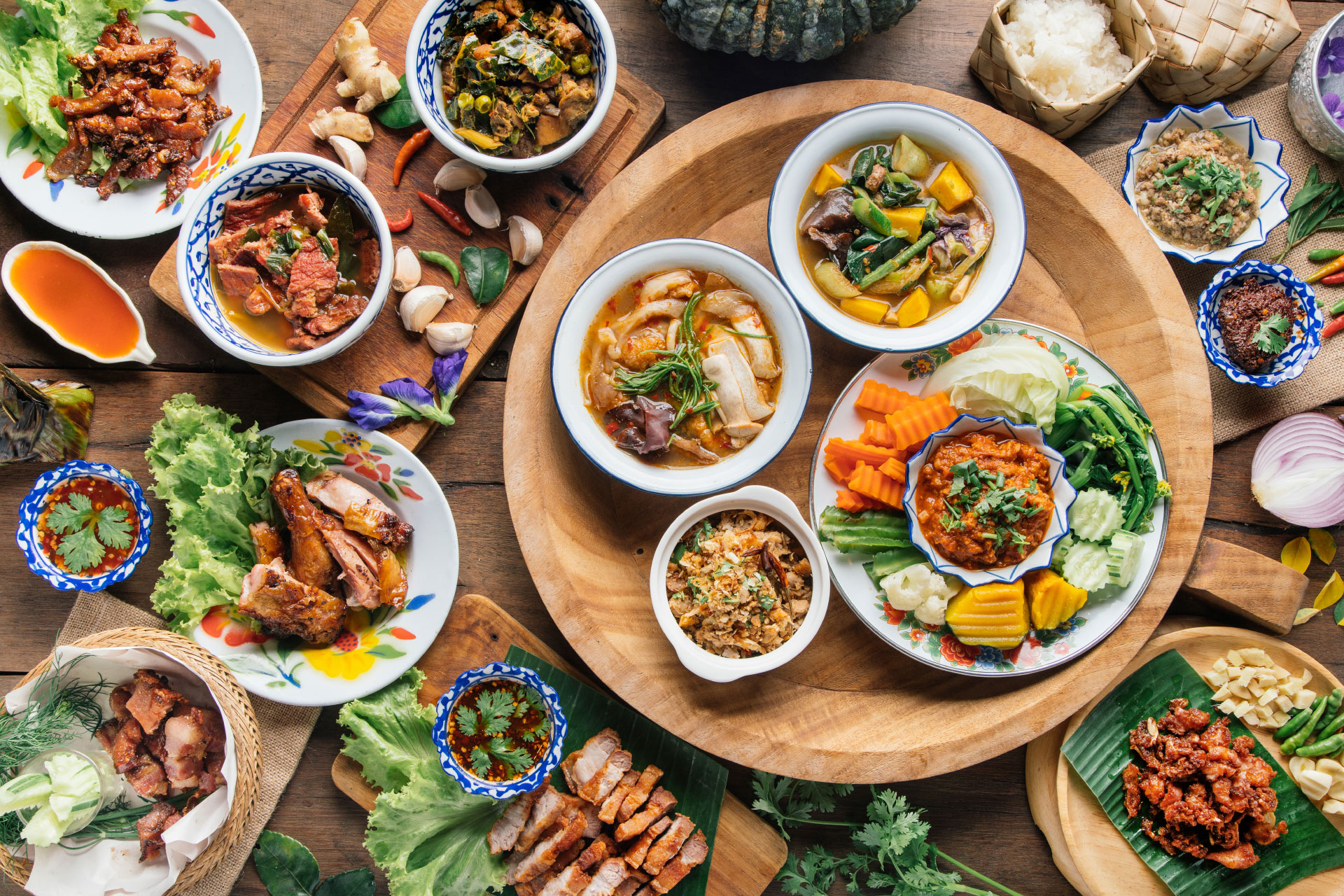 A Thai cuisine cookbook cover showing fresh herbs, curries, noodles, satay, and colorful street-style dishes.