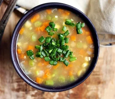 A bowl of clear vegetable soup with carrots, mushrooms, cabbage, spinach, and fresh herbs in a light golden broth.