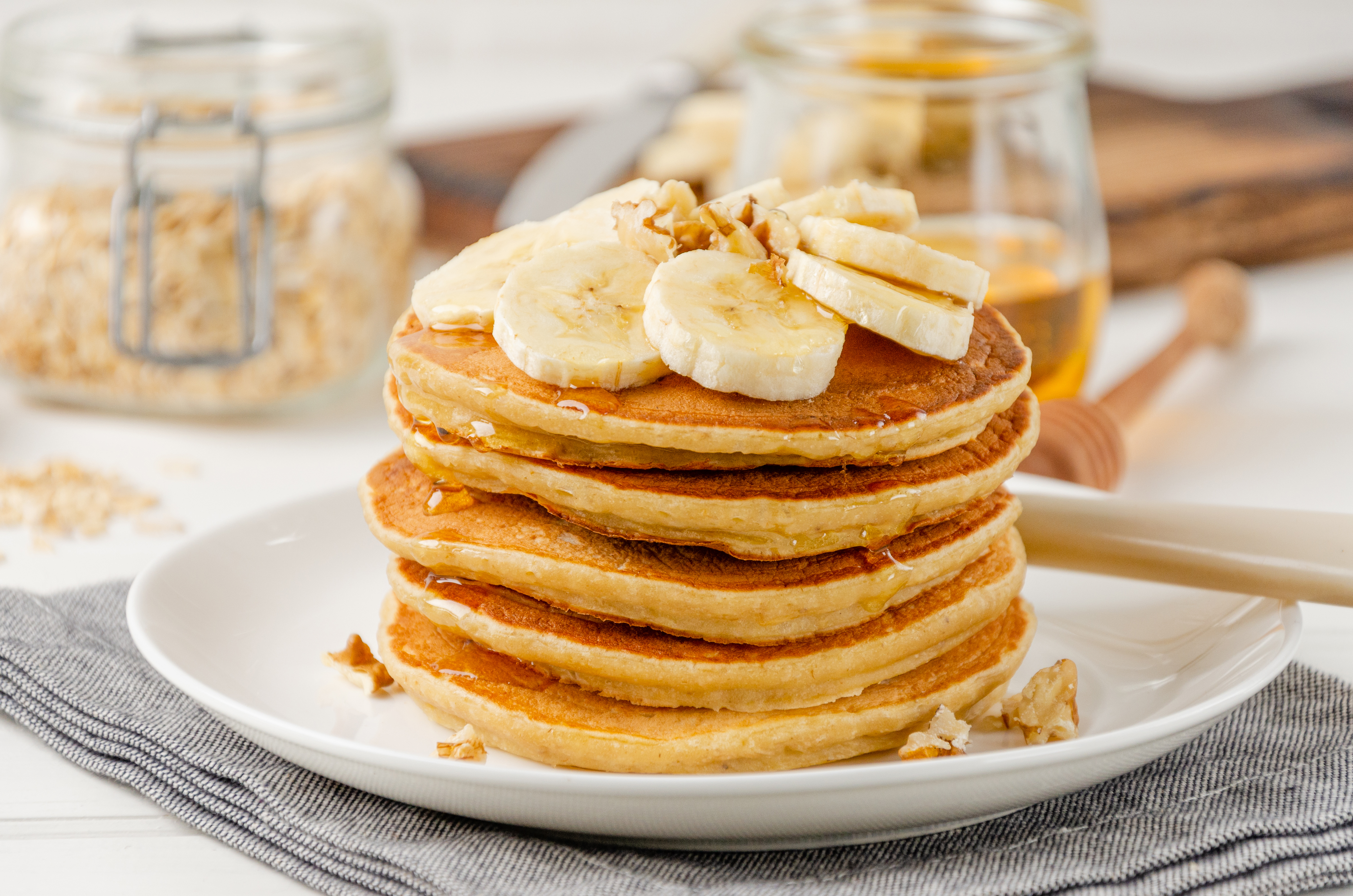 A stack of golden oatmeal pancakes with sliced banana and maple syrup.