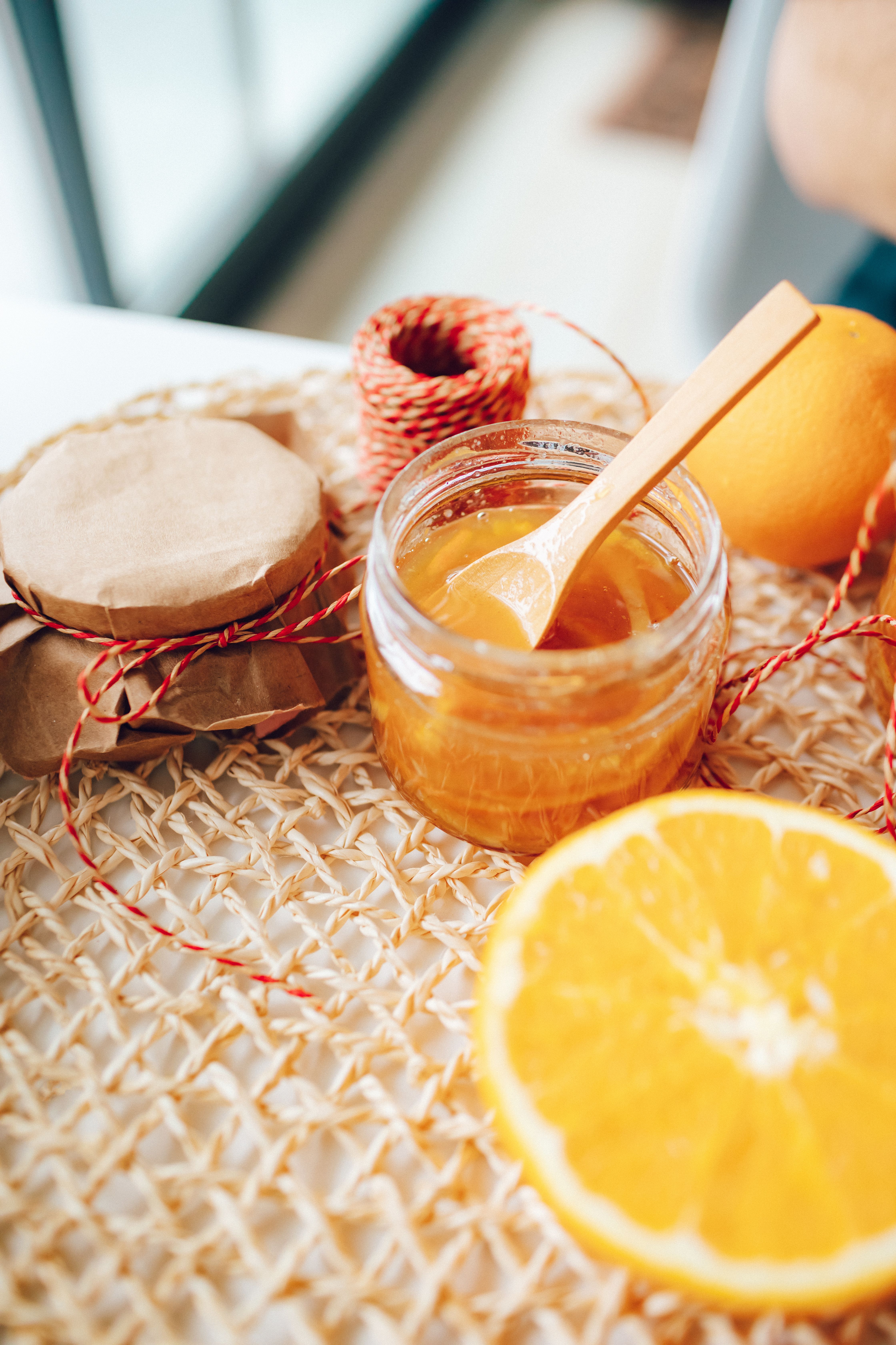 Bright golden lemon jam in a glass jar surrounded by fresh lemons, lemon zest and slices of toasted bread.