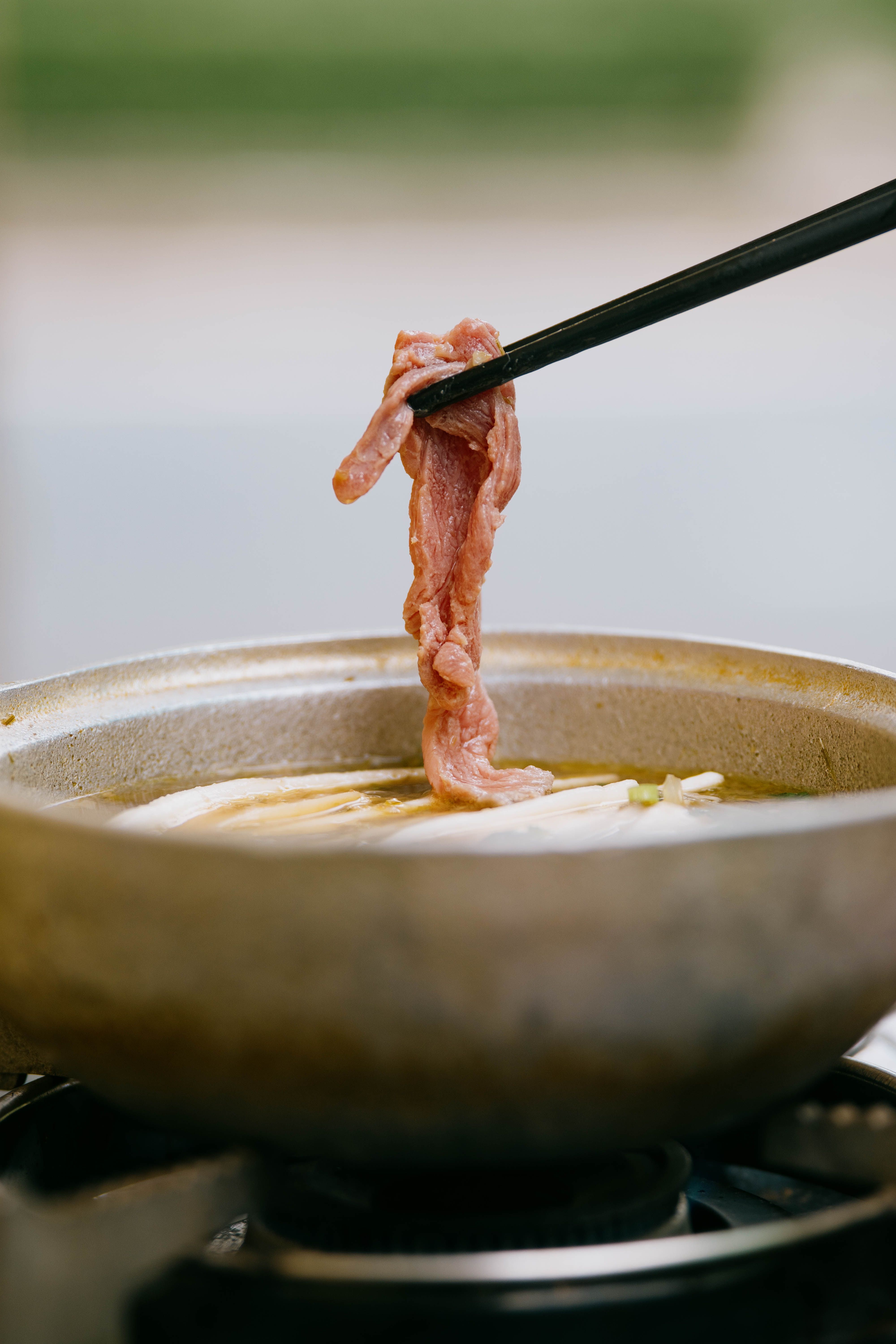 A steaming Japanese shabu shabu hot pot on a table surrounded by platters of thinly sliced beef, mushrooms, tofu, and fresh vegetables.