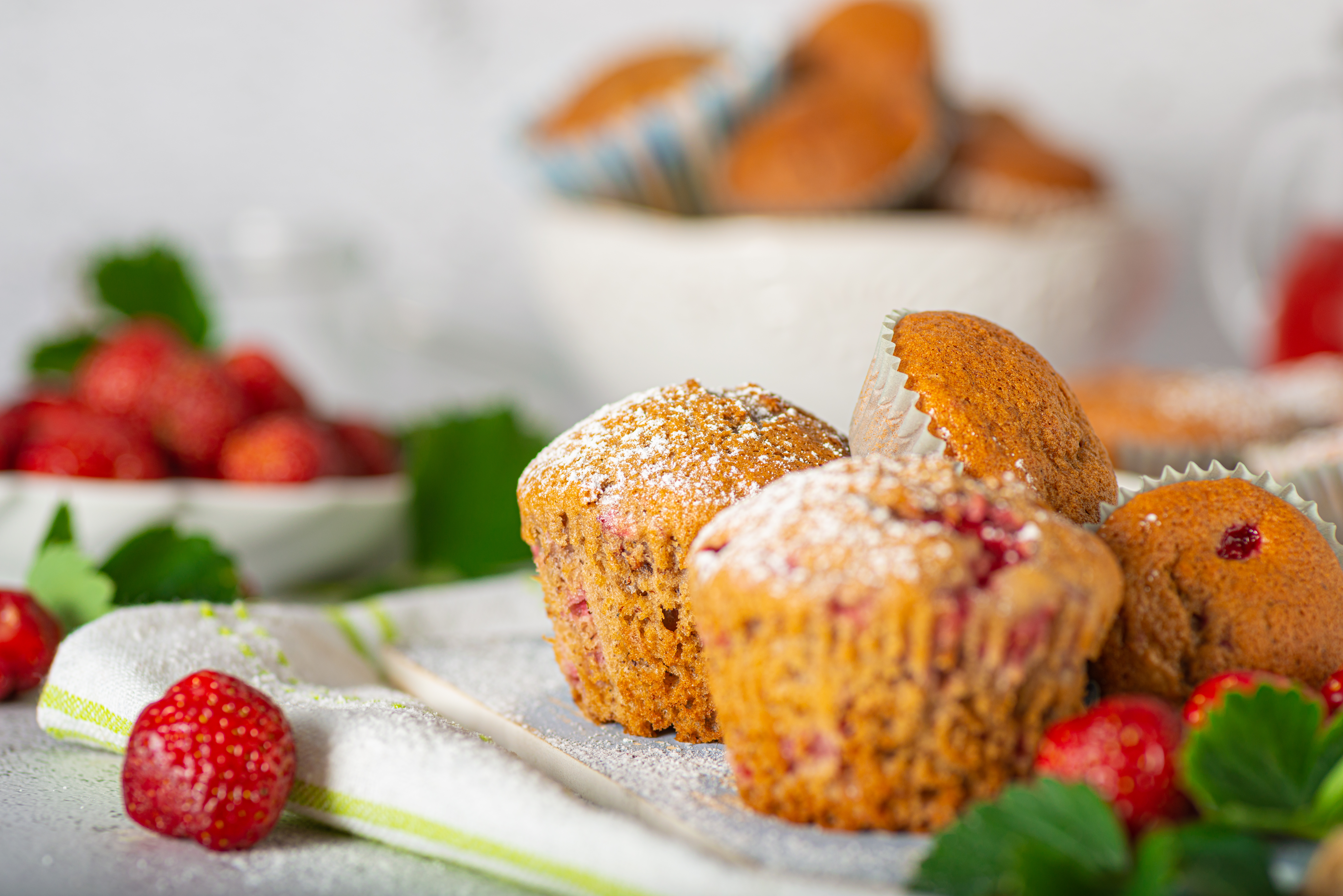 A tray of freshly baked strawberry muffins with golden domed tops, coarse sugar sparkle, and juicy pink strawberry pieces peeking out.