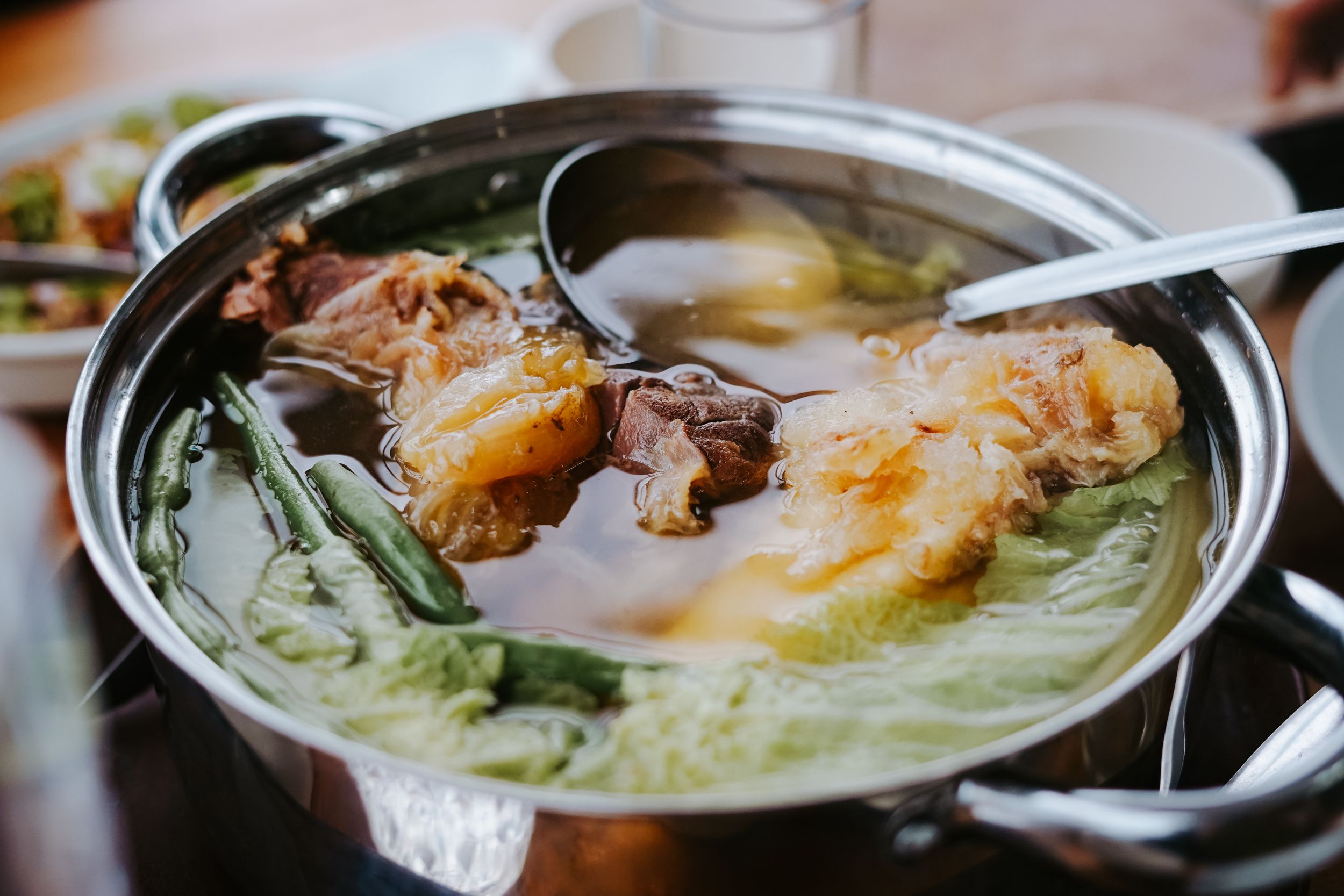 A steaming bowl of Nilagang Baka Filipino beef soup with corn, potatoes, and cabbage in a clear broth.