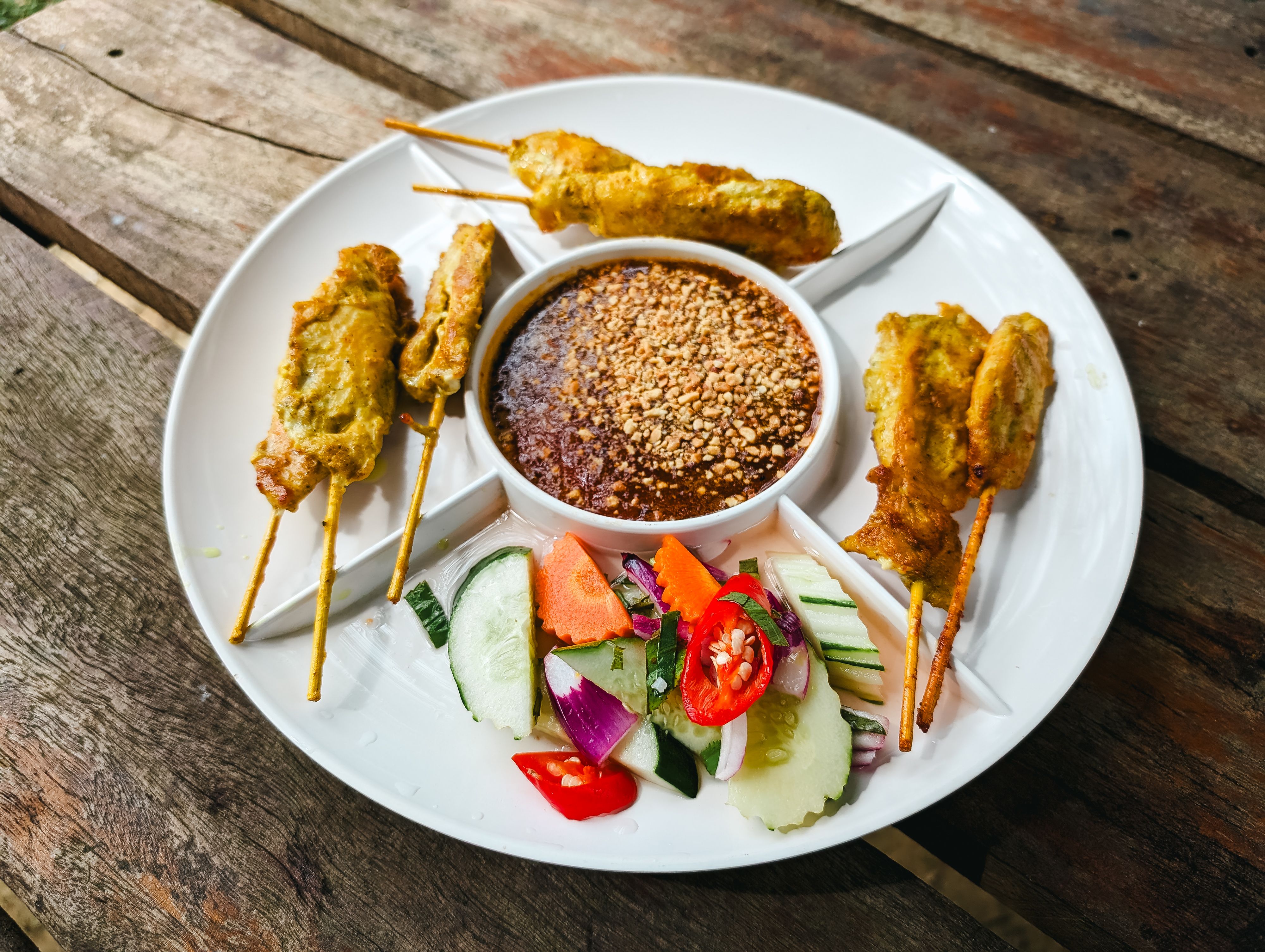 Creamy satay sauce topped with chopped peanuts and fresh coriander in a small serving bowl.