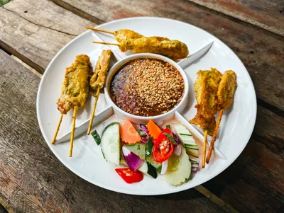 Creamy satay sauce topped with chopped peanuts and fresh coriander in a small serving bowl.