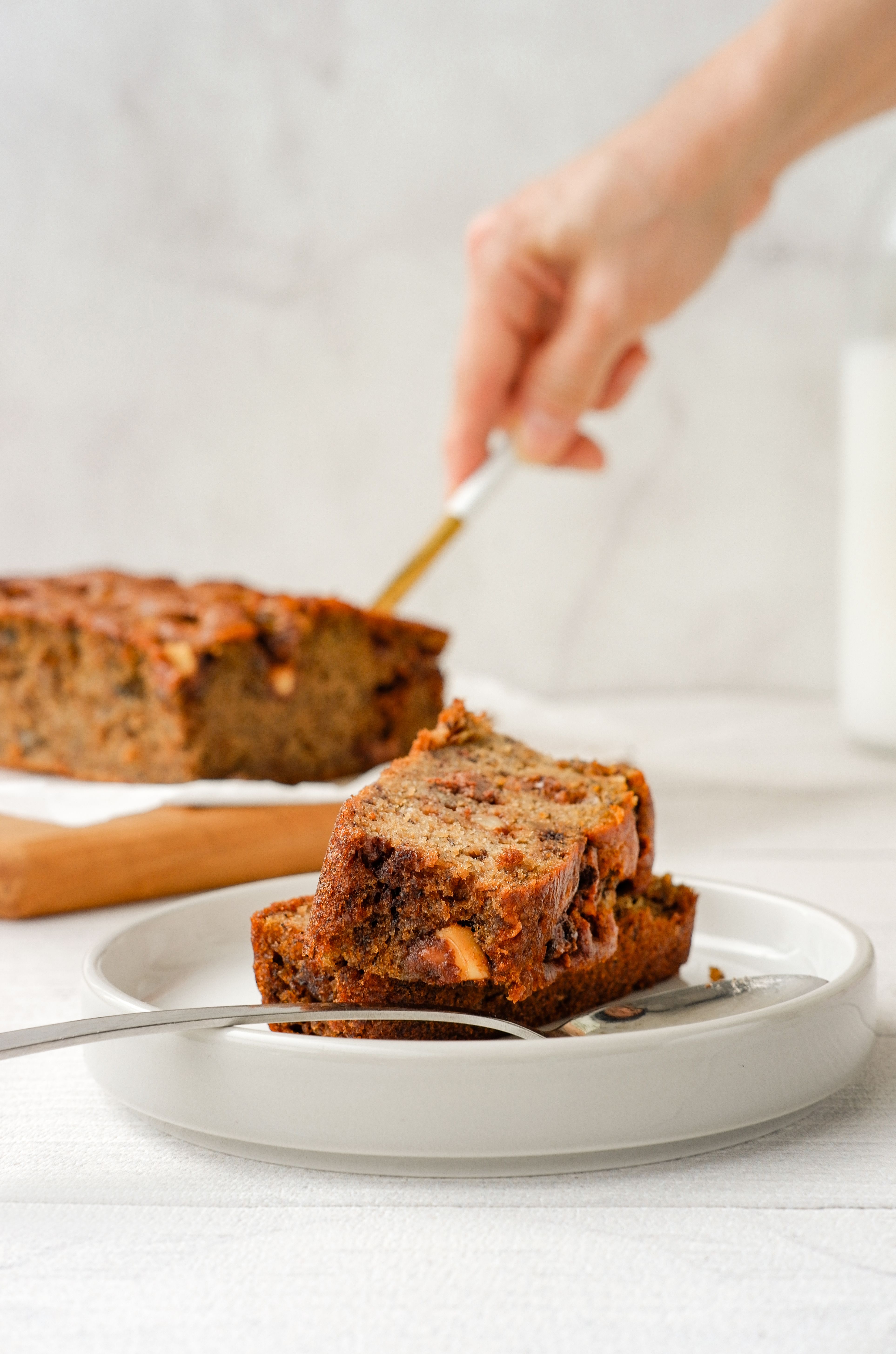 Moist gluten-free banana bread sliced on a wooden board with ripe bananas and dark chocolate pieces.