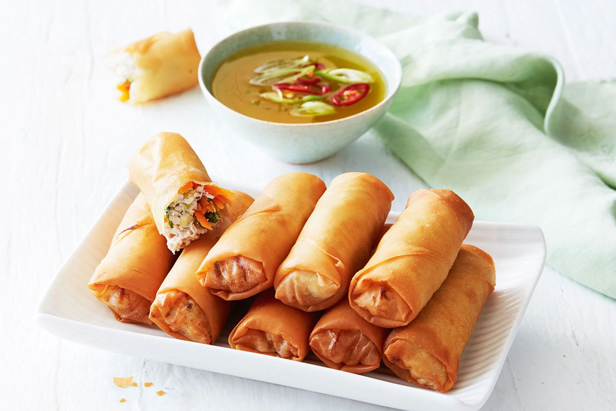 Golden fried chicken spring rolls cut open to show a spiced chicken and vegetable filling.